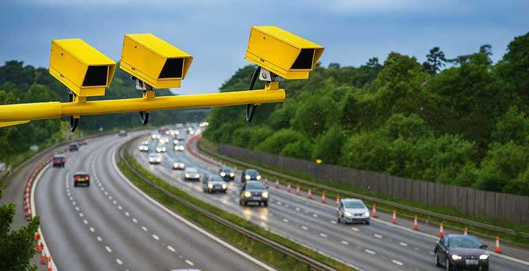 Yellow AI speed camera monitoring vehicles on a UK motorway under the August 2025 speeding fine rules, with penalties up to £450 for repeat offenders.