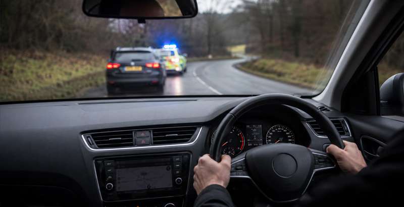 Right-hand drive car on a UK road with police vehicle and new driving laws sign highlighting tougher penalties